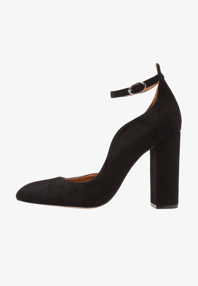 Chaussure à talon haut en daim noir avec une pointe effilée, une sangle à la cheville avec des éléments en acier inoxydable et un large talon carré. Texture lisse sur l'ensemble.