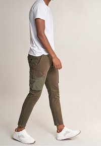 Khaki spodnie cargo z bocznymi kieszeniami, w dopasowanym kroju i kontrastującym zielonym materiałem. Połączone z białym t-shirtem z krótkim rękawem i białymi trampkami.