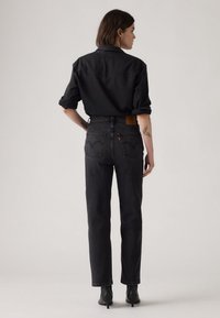 Zwarte denim jack met opgerolde mouwen en hooggetailleerde zwarte jeans. Kenmerken zijn een leren achterpatch en opvallende achterzakstiksels.