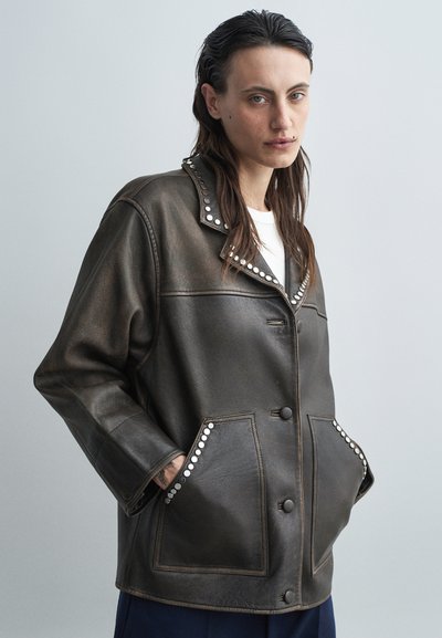 Veste en cuir marron foncé avec un col revers, ornée de clous en argent le long des bords et des poches, offrant une coupe décontractée et une fermeture à bouton.