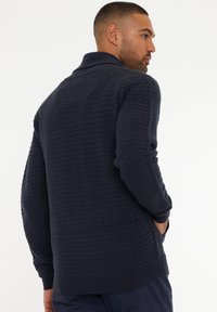 Suéter de punto azul marino con un patrón texturizado, que presenta un cuello doblado y puños acanalados. Corte casual con bolsillos laterales.