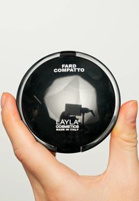 Custodia per cipria compatta nera con superficie riflettente, con la scritta "FARD COMPATTO" e "LAYLA COSMETICS MADE IN ITALY" stampate in bianco.