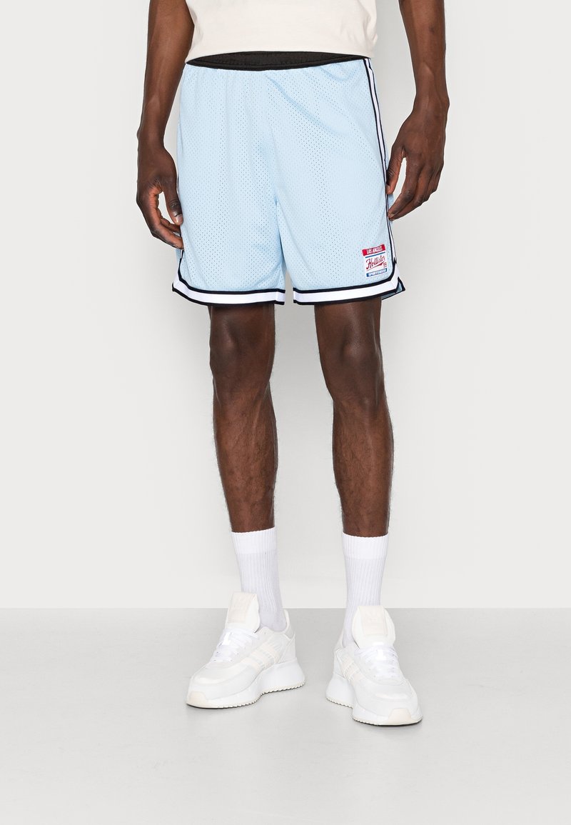 Ljusblå mesh-träningsshorts med svarta detaljer och en logotypapplikation. Bärs med vita strumpor och vita sneakers, vilket visar en avslappnad sportig stil.