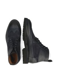 Par de botas de tobillo brogue de cuero y ante azul oscuro con suelas de goma gruesas y cordones, mostradas desde vistas superiores y laterales.