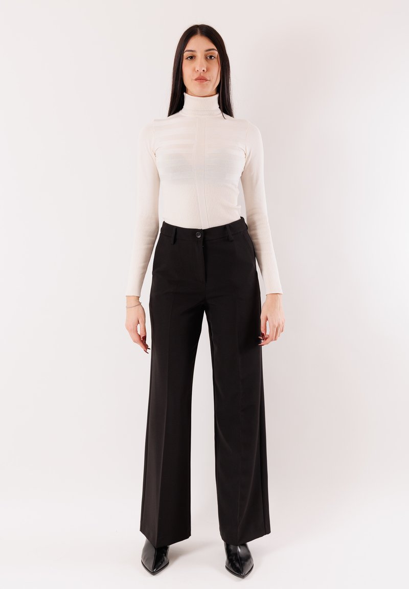 Collo alto bianco e pantaloni neri a gamba larga a vita alta. Tessuto liscio con silhouette aderente e chiusura con bottoni in vita.