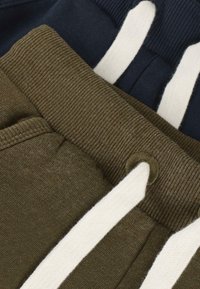 Nahaufnahme von zwei Paar Jogginghosen mit gerippten Elastikbund und weißen Kordeln, eine olivgrün und eine navy blau.