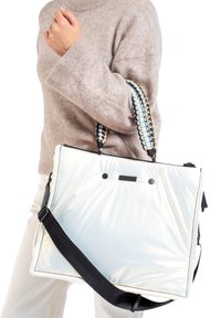 Sac fourre-tout brillant et blanc avec une forme structurée, doté d'une sangle noire, d'une poignée tissée multicolore et de deux accents en forme de points noirs.