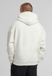 Witte hoodie met een ontspannen pasvorm, geribde manchetten en zoom. De achterkant heeft een minimalistisch ontwerp zonder zichtbare logo's of patronen.