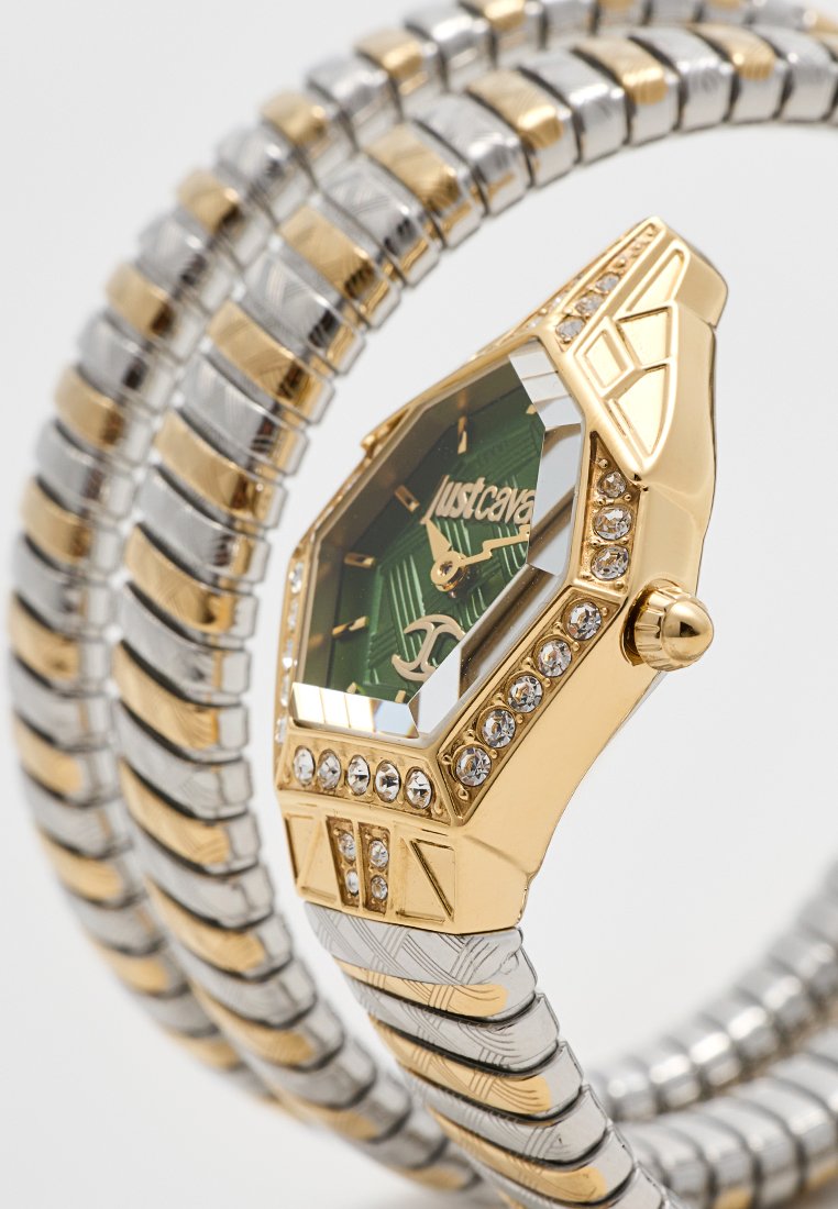 Reloj de pulsera metálico en oro y plata con esfera octagonal verde, acentos de cristal y detalles texturizados en la correa; presenta el nombre de la marca visible.