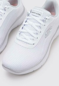 Scarpe da ginnastica in mesh bianche con suola in gomma liscia, design con lacci e sottili accenti argentati sulla suola intermedia e sul logo.
