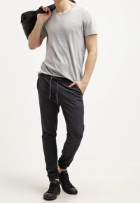 Šedé tričko volnějšího střihu ve spojení s černými tepláky s elastickým pasem a dvěma bočními kapsami. Černé tenisky doplňují vzhled.