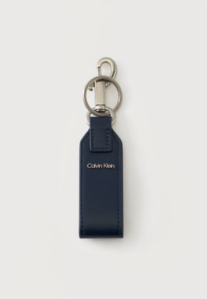 Porte-clés Calvin Klein en cuir bleu marine avec anneau et fermoir argentés sur un fond clair uni.