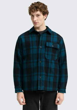 Blauw en zwart geruite flanellen overhemd met knopen, een kraag en een borstzak. Draagt over een zwart shirt, met een zachte textuur en een comfortabele pasvorm.