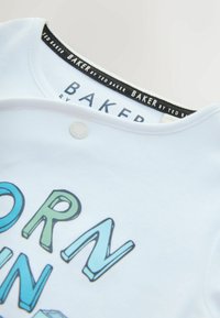 Witte katoenen t-shirt met een ronde halslijn. Bevat het label "BAKER by Ted Baker" en een kleurrijk tekstontwerp in groen en blauw. Drukknoopdetail.
