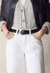 Črna usnjena jakna čez sivi volneni kardigan z gumbi, kombiniran z belimi kavbojkami z visokim pasom in črnim pasom s srebrno sponko.