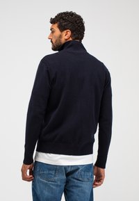 Navy Strickpullover mit hohem Kragen, gerippten Bündchen und Saum. Getragen mit hellblauen Jeans, die eine glatte Textur und eine figurschmeichelnde Passform zeigen.