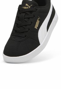 Svart sneakers i tyg, med en vit sidrand, snörning framtill, texturerad sula och guldiga logografik. Klassisk stil.