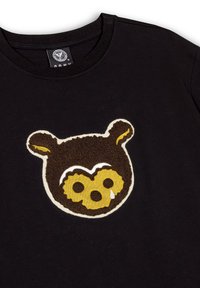 Czarna bawełniana koszulka z teksturowanym wzorem przedstawiającym niedźwiedzia w kolorze brązowym i żółtym, z białymi akcentami oraz detalem w postaci rozdarcia, umieszczonym centralnie.