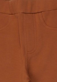 Rostfarbene Hose mit glatter Textur, ausgestattet mit gesteppten Details, einem flachen Taillenbund und einem Design mit einer einzelnen Tasche.