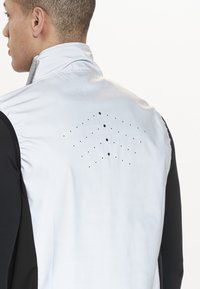Graues Sportweste mit schwarzen Seitenpaneelen. Verfügt über einen hohen Kragen und ein perforiertes Muster auf der Rückseite zur Belüftung. Glatte Textur.