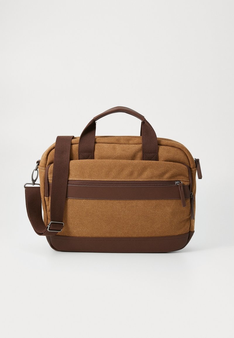 Serviette marron en toile et cuir avec doubles poignées, poche avant zippée et bandoulière réglable sur un fond uni.