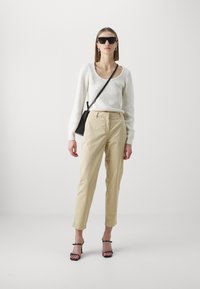 Balts ribots džemperis, bēšu augstās jostas bikses, melnas siksnu kurpes ar papēdi un lielas melnas saulesbrilles. Vienkārša melna crossbody soma.