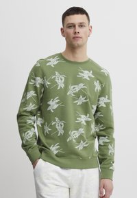Groene sweatshirt met een wit bloemenpatroon. Beschikt over lange mouwen, ronde hals en geribbelde manchetten. Gemaakt van zachte, gestructureerde stof.
