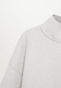 Top de manga larga de tejido suave en gris claro, con cuello alto y detalles de costura visibles en el hombro y la manga.