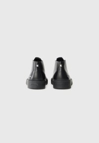 Botas de tobillo de cuero negro con un diseño elegante, punta redondeada y suela de goma texturizada. Presentan acentos plateados en el tacón.