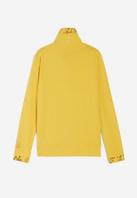 Maglia gialla a maniche lunghe con collo alto, caratterizzata da accenti floreali sul collo e sui polsini. Tessuto morbido e liscio.