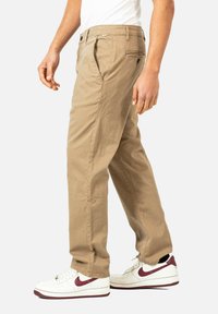 Khaki Chinos mit geradem Schnitt und Vorderfalten, ausgestattet mit Seiten- und Gesäßtaschen, kombiniert mit weißen und burgunderfarbenen Sneakers.