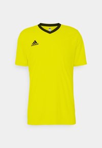 Camiseta deportiva amarilla con un cuello en V negro, mangas cortas y un logo negro de Adidas en el lado izquierdo del pecho. Textura de tela suave.