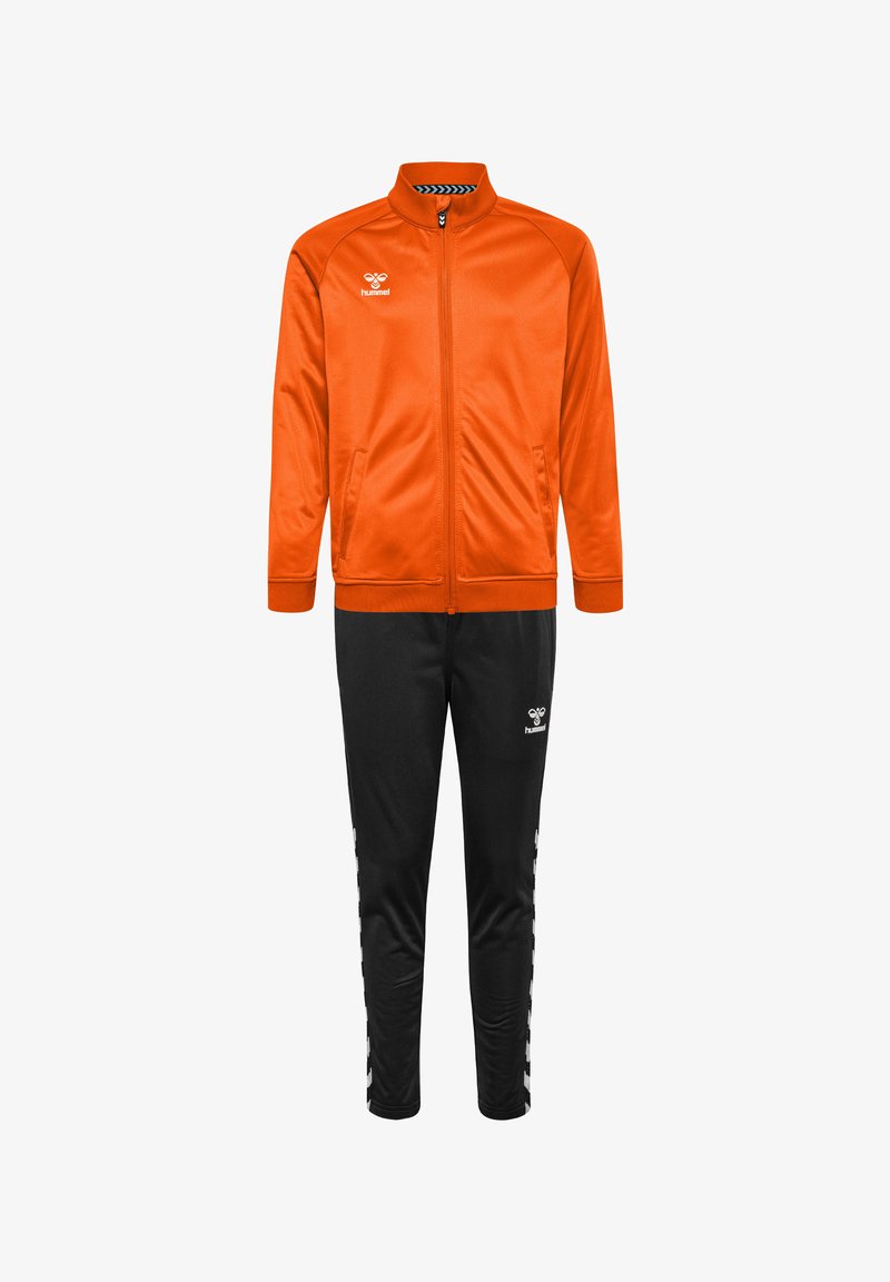 Pomarańczowa sportowa kurtka na zamek z czarnymi spodniami dresowymi. Kurtka ma wysoki kołnierz i kieszenie; spodnie mają boczne pasy i logo.