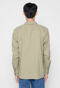 Hell olivgrünes Langarmhemd mit klassischem Kragen, geknöpften Manschetten und glattem, leichtem Stoff. Rückansicht zeigt eine lockere Passform.