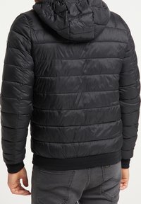 Schwarze Steppjacke mit strukturierter Oberfläche, mit Kapuze, horizontalen Nähten und gerippten Bündchen an Ärmeln und Saum.