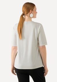 Lys grå kortærmet bluse med en afslappet pasform, glat tekstur og rund hals. Stylet med sorte bukser og store hvide runde øreringe.