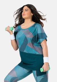 Conjunto de ropa deportiva que presenta una camiseta verde azulado con patrones geométricos y leggins a juego, ambos fabricados con un tejido ligero y elástico. Sostiene mancuernas verdes.