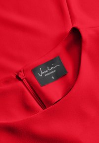 Indumento rosso con una texture liscia, chiusura con zip e etichetta nera con "Vaschö Stockholm" e taglia "S". Design semplice con scollatura rotonda.