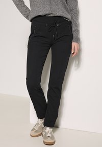 Zwarte joggingbroek met een trekkoord in de taille, twee met rits afgesloten zakken en een tapered fit. Gemaakt van zachte, rekbare stof voor comfort.