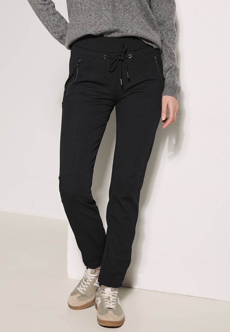 Zwarte joggingbroek met een trekkoord in de taille, twee met rits afgesloten zakken en een tapered fit. Gemaakt van zachte, rekbare stof voor comfort.