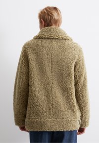 Faux shearlingjacka i olivgrön med krage, texturerad yta och två sidoventiler med nedtonade hårdvaruakcent.