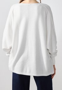 Vit oversized tröja med en texturerad stickning, bred båtutskärning och sänkta axlar, kombinerad med mörkblå jeans.