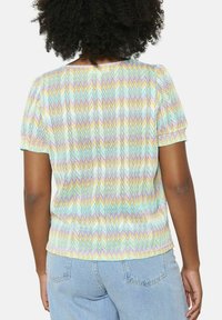 Blusa corta y colorida de manga corta con un patrón de zigzag en tonos pastel de azul, amarillo, rosa y blanco, hecha de una tela texturizada.