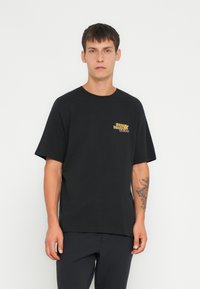 Zwarte katoenen T-shirt met korte mouwen, een ronde halslijn en een kleurrijk grafisch logo op de linkerborst. Gladde textuur.