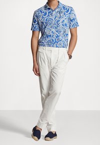 Blå piké med paisleymönster och kort ärm, vita plissébyxor och blå espadriller med jute-detaljer. Slätt tyg och avslappnad passform.