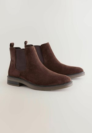 Bottines en daim brun avec des panneaux élastiques sur les côtés, bout rond et un petit talon carré. Présente des coutures contrastées le long de la semelle.
