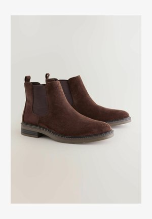 Bottines en daim brun avec des panneaux élastiques sur les côtés, bout rond et un petit talon carré. Présente des coutures contrastées le long de la semelle.