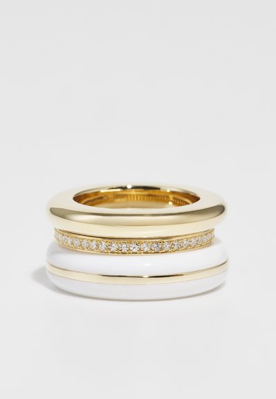 Guld- og hvide stablede ringe; en glat guld ring, en hvid ring med en guldstribe og en tredje prydet med klare sten.