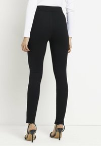 Zwarte legging met een gladde, rekbare stof, een hoge tailleband en een slanke pasvorm, gecombineerd met zwarte sandalen met hak.