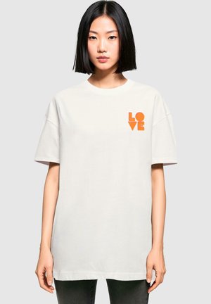 White cotton t-shirt with short sleeves featuring a bright orange "LOVE" graphic on the left chest. Relaxed fit and plain design.